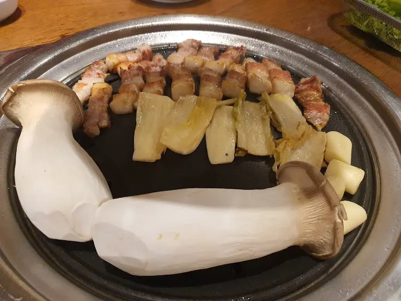 불판 위에 올려진 삼겹살, 김치, 버섯