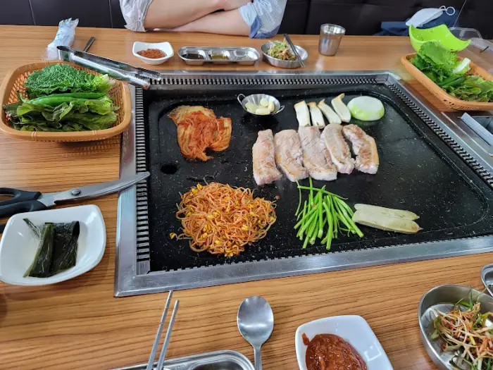불판 위에 삼겹살, 김치, 콩나물, 미나리 등이 놓여있는 모습