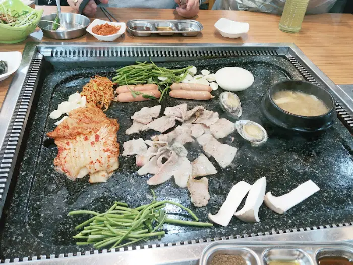 삼겹살, 전복, 소시지, 버섯 등이 불판 위에서 익어가는 모습