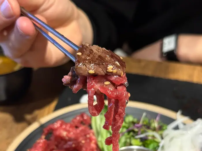 집게로 집어 올린 잘 구워진 소고기 한 점. 육즙이 풍부해 보인다.