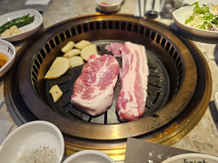 잘 구워진 삼겹살 조각과 곁들임 채소, 감자 등이 불판 위에 놓여 있다.