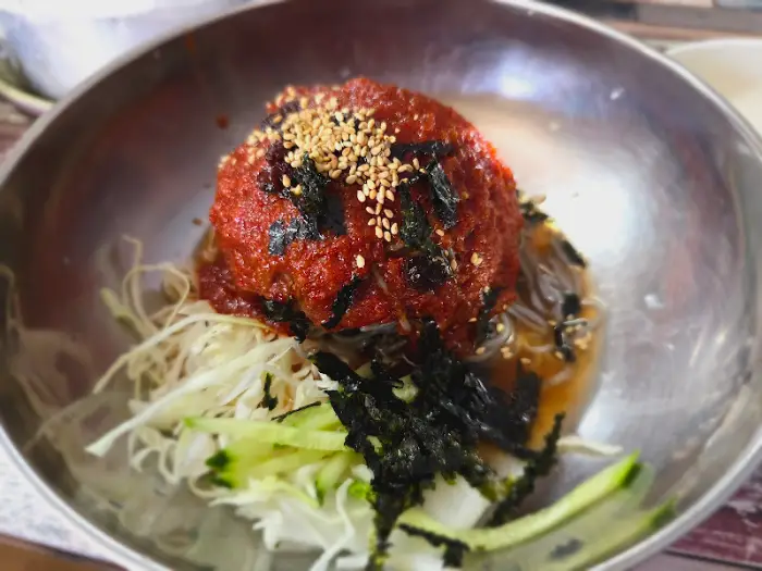 메밀면 위에 붉은 양념과 김가루, 깨가 얹어져 있는 비빔 막국수의 클로즈업