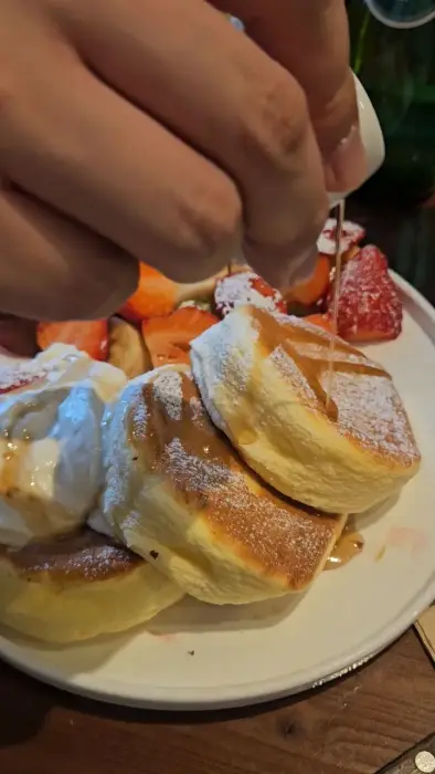 젠젠 수플레 팬케이크 위에 시럽을 뿌리는 모습. 퐁신한 수플레의 질감이 돋보인다.