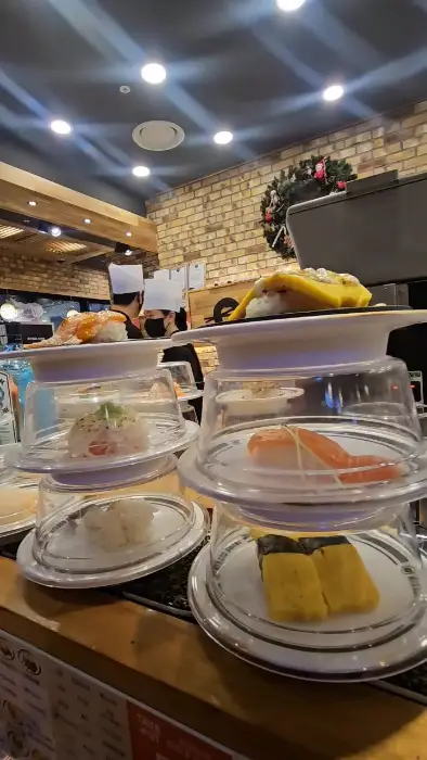 여러 겹의 접시 위에 각기 다른 초밥들이 놓여 있다. 노란 계란 초밥과 붉은 연어 초밥이 보인다.