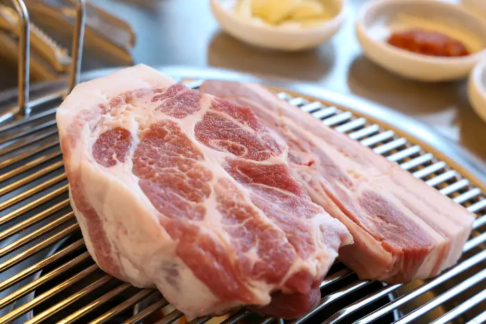 신선한 흑돼지 오겹살 덩어리가 불판 위에 놓여 있다