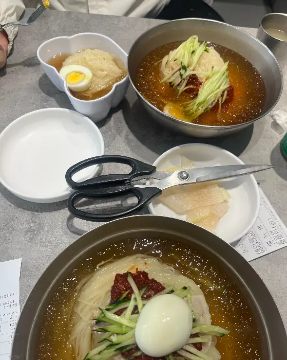 테이블 위에 차려진 밀면과 비빔밀면, 그리고 만두. 여러 가지 메뉴를 함께 즐기는 모습입니다.