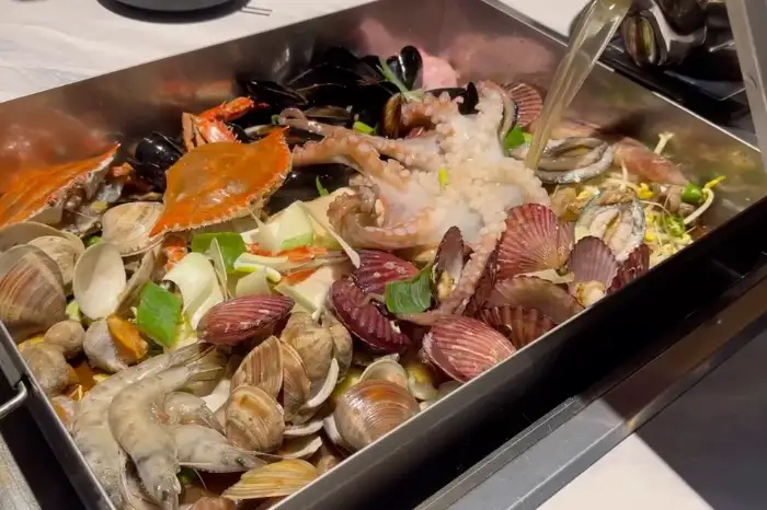 커다란 찜기 안에 문어, 조개, 새우, 게 등 다양한 해산물이 가득 담긴 모습