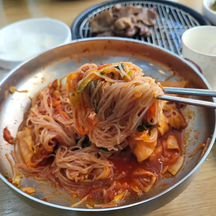 젓가락으로 집어 올린 냉면. 가늘고 하얀 면발에 빨간 양념이 묻어 있다.