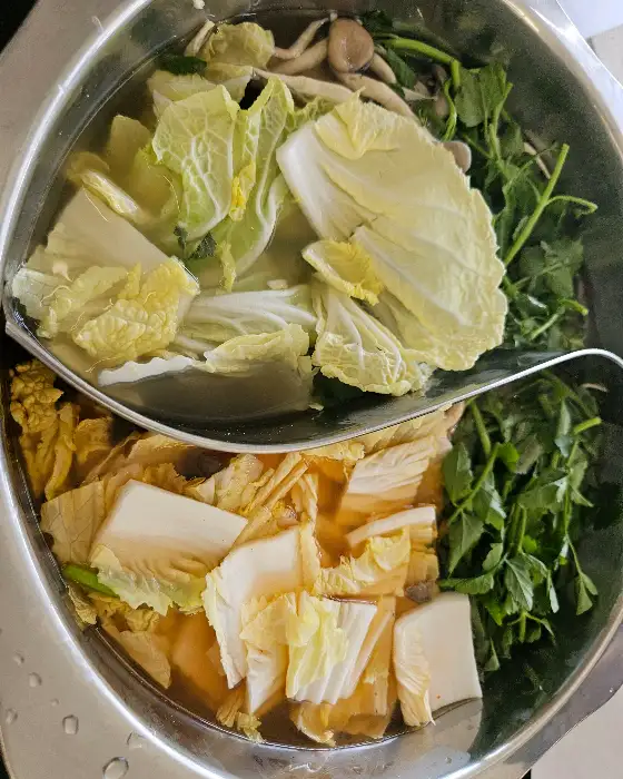 샤브샤브 냄비에 맑은 육수와 신선한 채소가 담겨 있는 모습