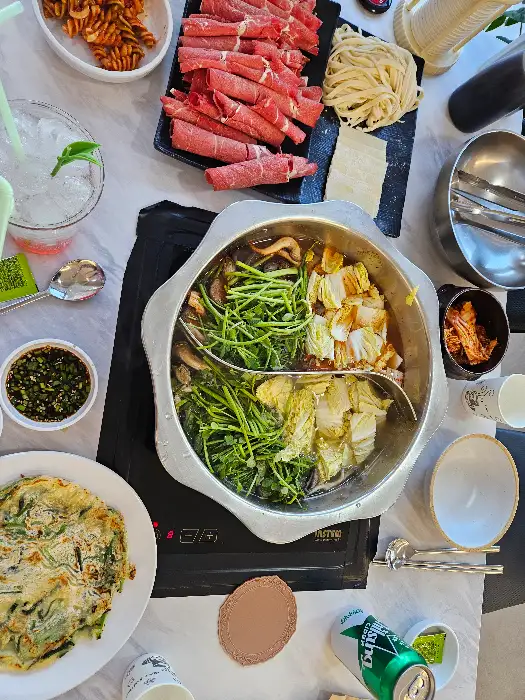 테이블 위에 차려진 샤브샤브 재료, 부침개, 소스 등 다양한 음식들