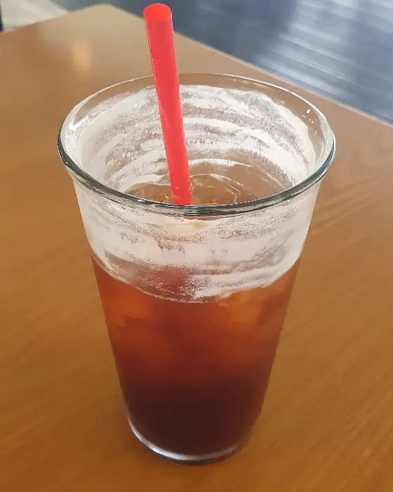 얼음이 가득한 투명한 컵에 담긴 아이스 아메리카노와 붉은색 빨대가 보인다.