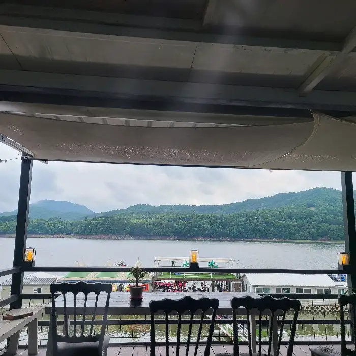 테라스 테이블에 놓인 의자들과 그 뒤로 펼쳐진 장성호의 풍경이 보인다.