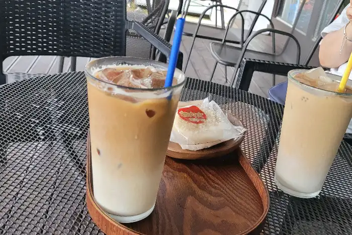 두 잔의 음료와 디저트가 놓인 테이블과 뒤로 보이는 야외 좌석의 모습.