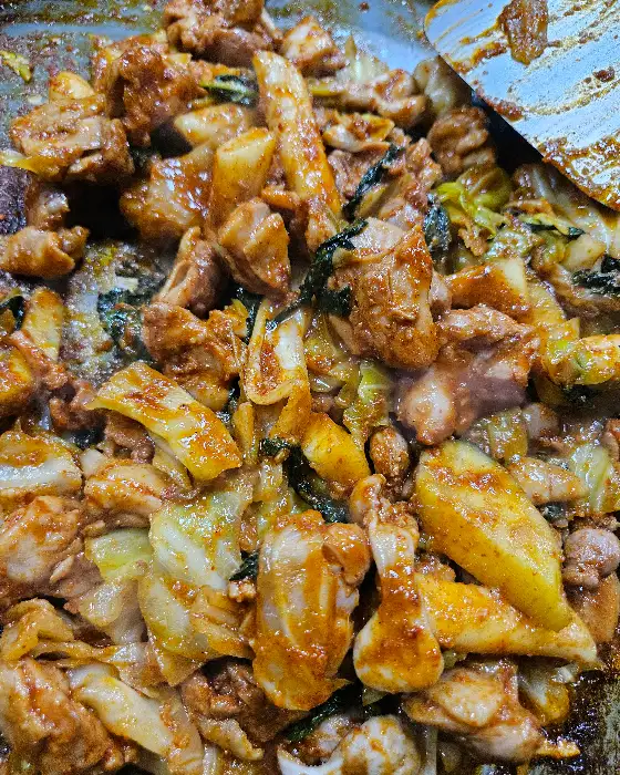 철판 위에서 익어가고 있는 닭갈비에 떡과 채소가 함께 버무려진 모습