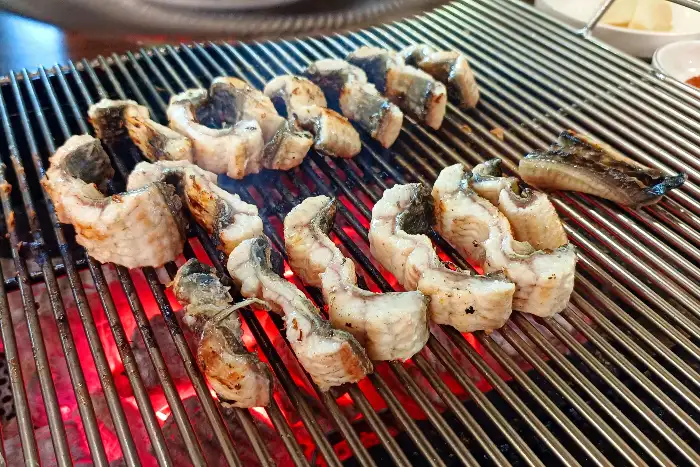 숯불 위에서 노릇하게 구워지는 장어 조각들