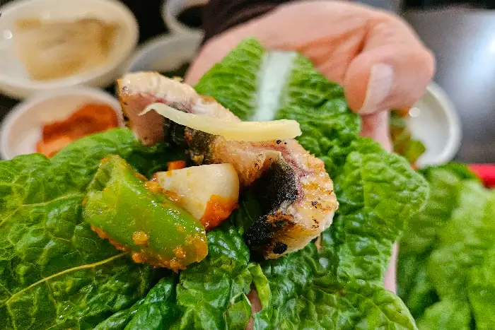상추쌈 위에 올려진 장어구이 한 점과 곁들임 재료