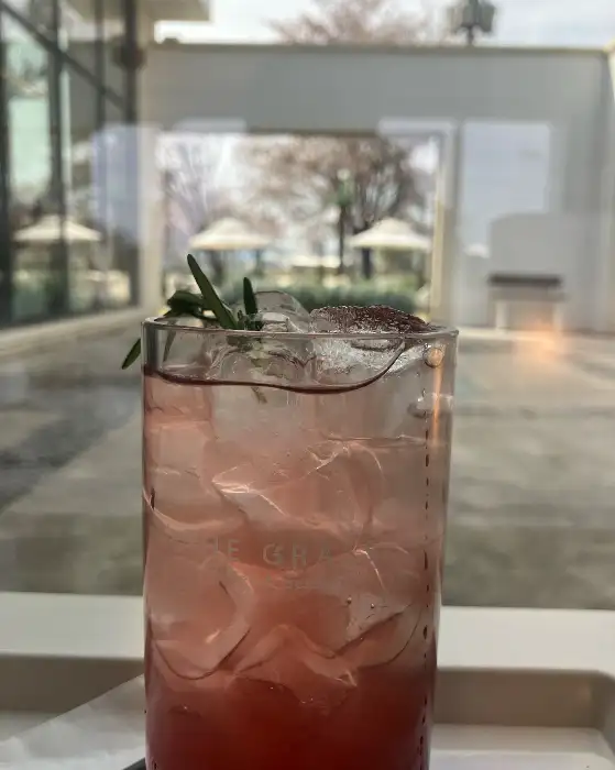 투명한 잔에 담긴 핑크빛 음료와 얼음, 그리고 허브가 장식되어 있습니다.