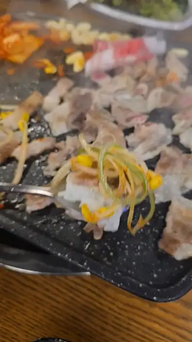 불판 위에서 함께 구워지고 있는 대패삼겹살, 콩나물, 김치 등