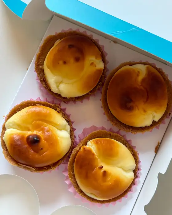 종이 컵케이크 틀에 담긴 네 개의 치즈 타르트. 윗면에는 부드럽게 구워진 치즈 필링이 얹어져 있다.