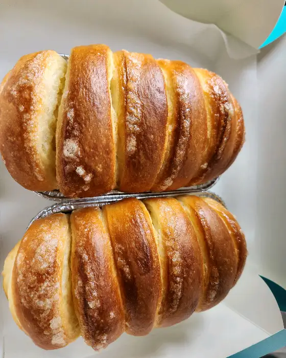 알루미늄 트레이에 담긴 두 개의 버터모닝이 겹쳐져 있다. 빵 표면에 설탕 결정이 살짝 보인다.