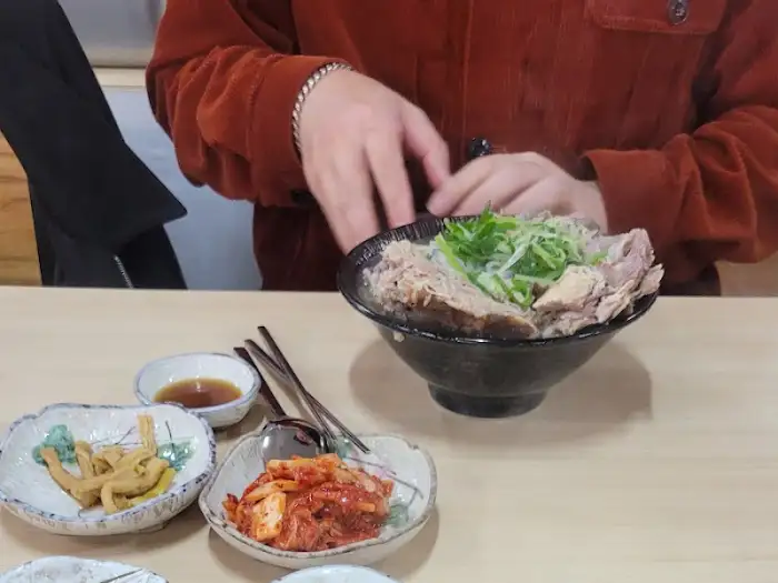 테이블에 놓인 접짝뼈국과 밑반찬들. 젓가락이 국물 안의 고기를 집고 있다.