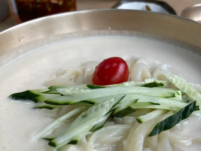 뽀얀 콩국수 위에 채 썬 오이와 방울토마토가 올려져 있습니다.