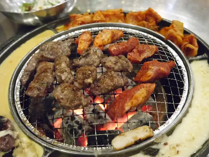 숯불 위에서 노릇하게 구워지고 있는 마늘 갈매기살과 곁들임 메뉴