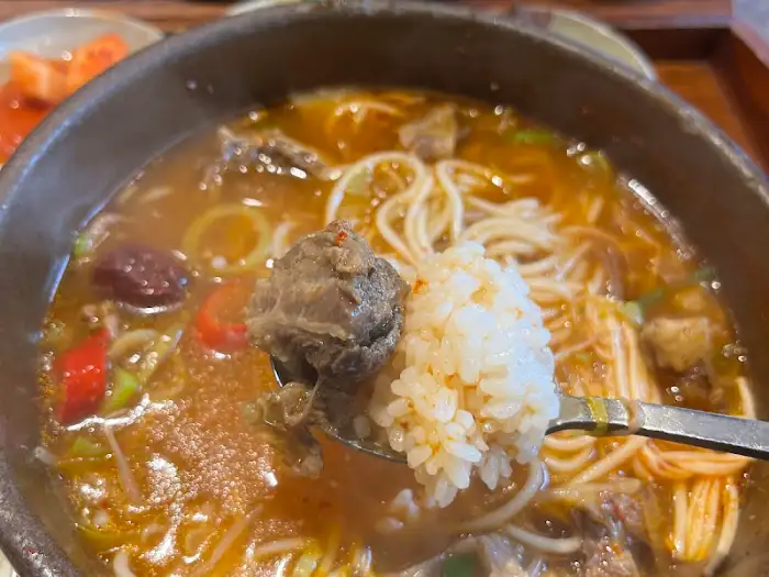 갈비탕에 밥과 큼지막한 갈비 한 점을 함께 뜨는 모습