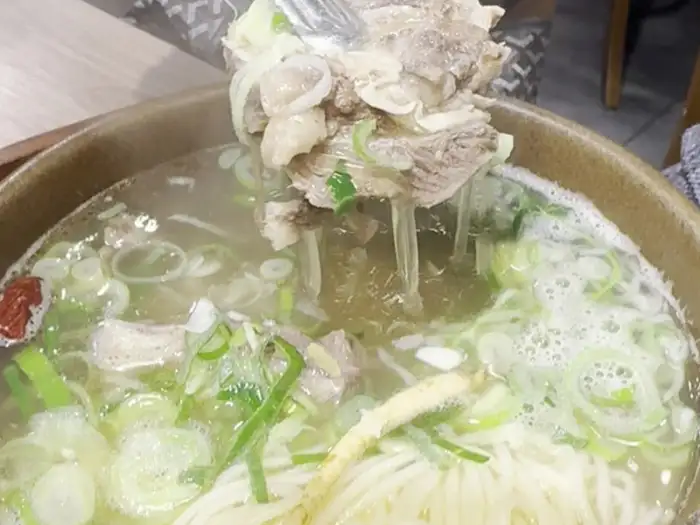 집게로 갈비탕 속 고기를 건져 올리는 모습