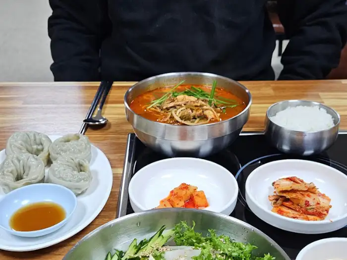 식탁 위에 차려진 닭개장, 밥, 만두, 깍두기, 김치