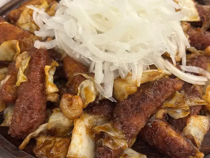 잘게 썰린 채소 위에 붉은 육류와 튀김이 어우러진 요리