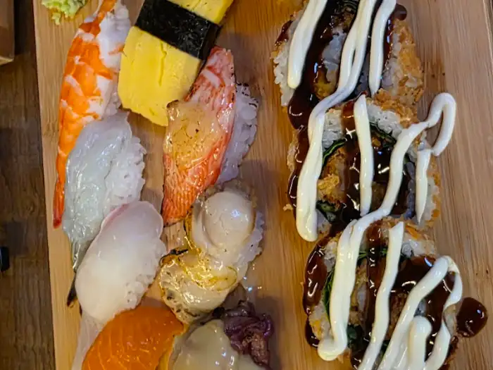 다양한 종류의 초밥이 한 접시에 담겨 있으며, 튀김 롤은 소스가 뿌려져 있다.