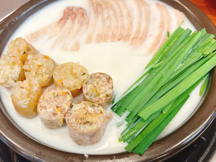 하얀 국물 베이스에 얇게 썬 고기, 부추, 그리고 여러 종류의 순대가 담겨 있는 사진.
