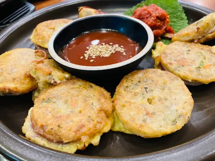 동그랗게 부쳐진 오징어순대와 매콤한 소스, 그리고 쌈 채소가 함께 담겨 있는 접시.