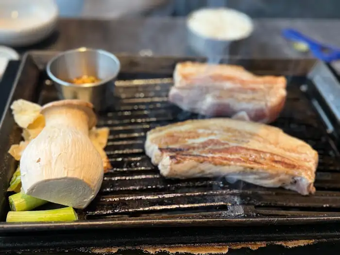 그릴 위에서 지글지글 익어가는 흑돼지 목살과 버섯
