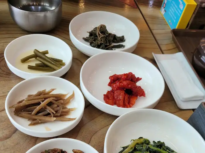 그릇에 담긴 붉은 양념의 더덕 무침과 다른 나물들