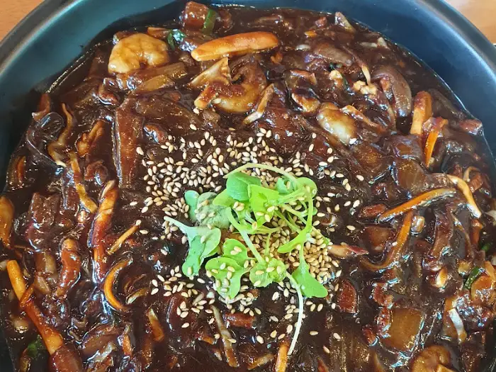 윤기가 흐르는 쟁반 짜장 위에 깨와 어린잎 채소가 올라가 있는 모습