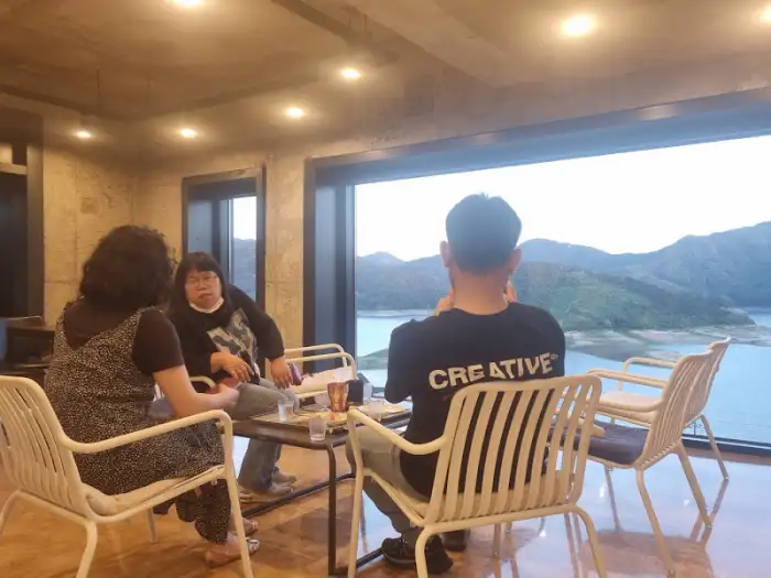 실내 좌석에 앉아 창밖을 바라보는 사람들. 테이블 위에는 음료와 빵이 놓여 있다.