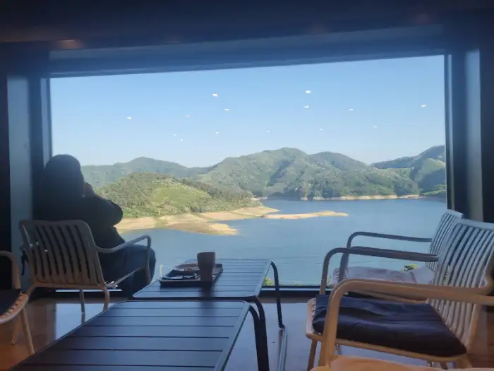 넓은 창을 통해 보이는 옥정호와 산자락의 풍경, 전경에는 테이블과 의자들이 놓여 있다.