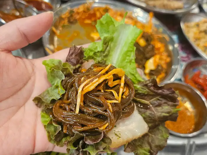 쌈 채소에 족발과 곁들임을 싸서 먹는 모습