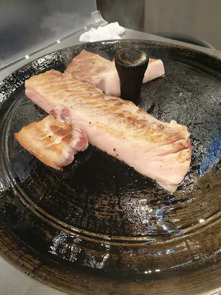 불판 위에서 천천히 익어가는 두툼한 삼겹살 덩어리