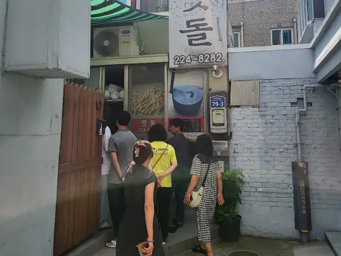 맷돌 돌리는 모습과 손님들이 줄 서 있는 입구 전경