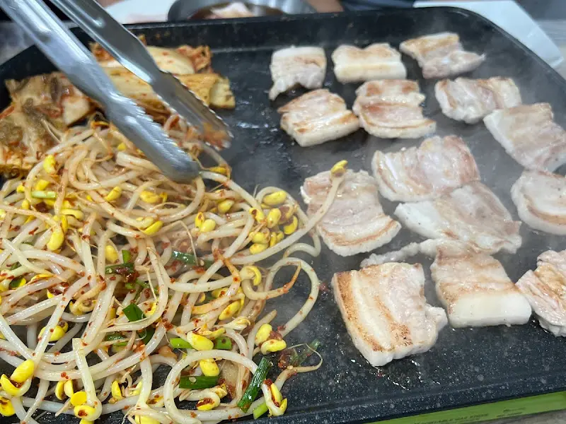 삼겹살과 콩나물이 불판 위에서 맛있게 익어가는 모습