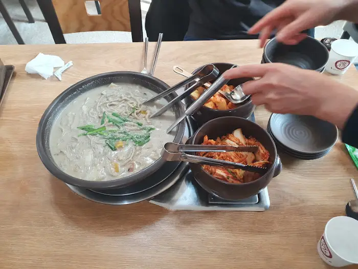 테이블에 차려진 콩국수와 김치, 젓가락 집게가 보인다.