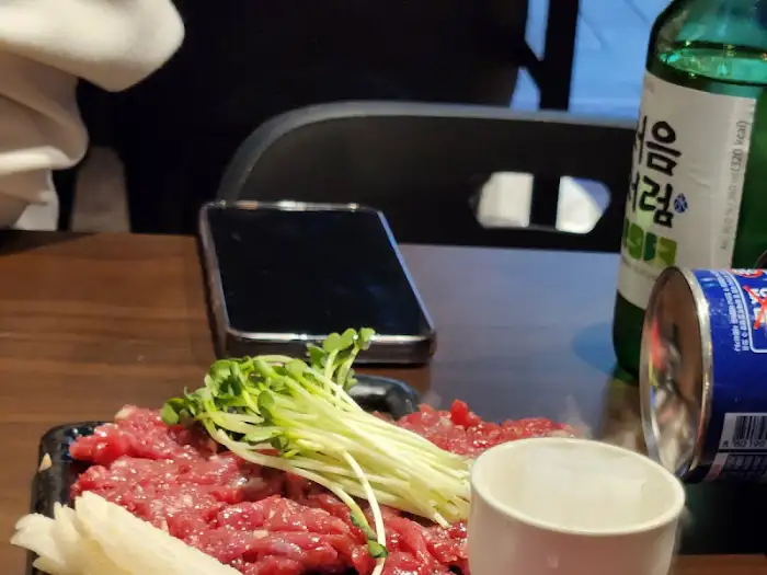 탁자 위에 놓인 휴대폰, 술병, 그리고 육회 접시