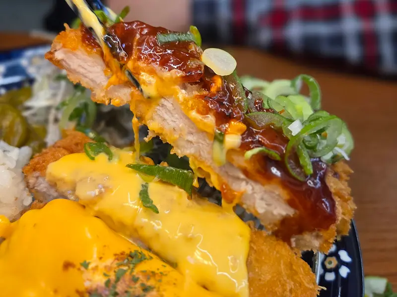 젓가락으로 돈카츠 한 점을 들어올린 모습. 윤기가 흐르는 소스와 촉촉한 돈카츠의 단면이 식욕을 자극한다.