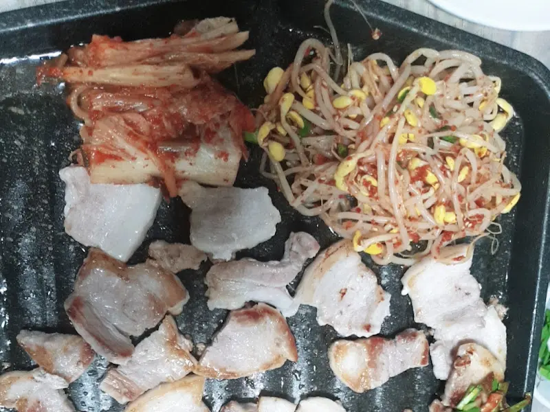불판 위에서 익어가는 삼겹살과 김치, 콩나물