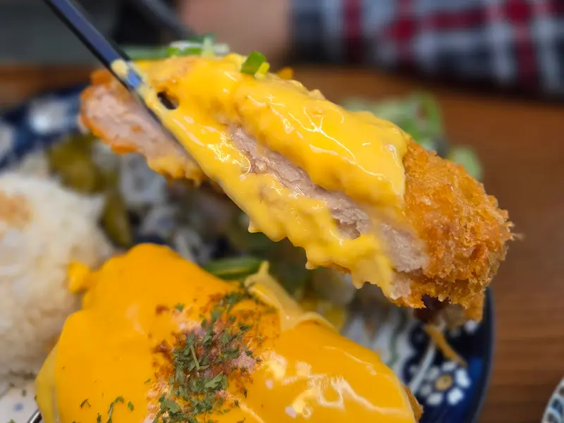 젓가락으로 치즈 돈카츠를 집어 올린 모습. 돈카츠 속 치즈가 녹아내려 먹음직스럽다.