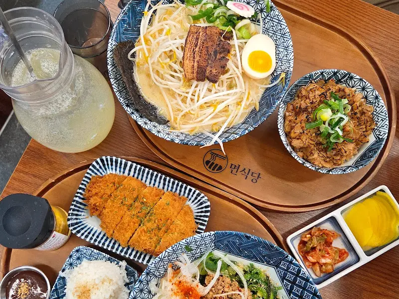 쟁반 위에 돈코츠라멘, 반반카츠, 김치미니부타동 등이 함께 놓여 있다. 푸짐한 양과 다채로운 메뉴 구성이 눈길을 사로잡는다.