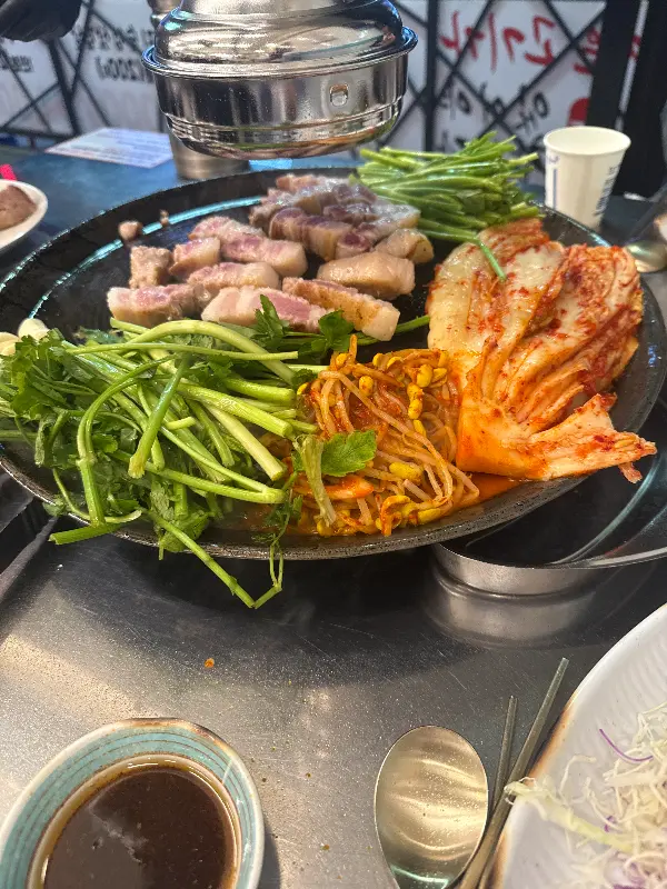 솥뚜껑 위에 삼겹살과 미나리, 김치가 함께 구워지는 모습